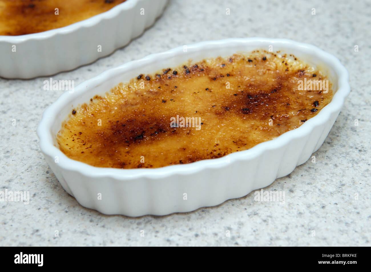 two creme brulee in small ramekins on a kitchen countertop Stock Photo