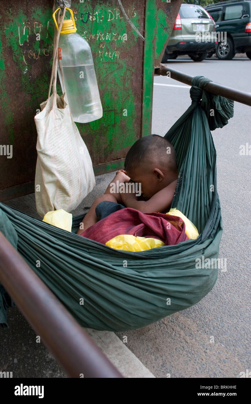 A young boy is sleeping in a hammock tied to a Cintri garbage collection cart on Norodom Boulevard in Phnom Penh, Cambodia. Stock Photo