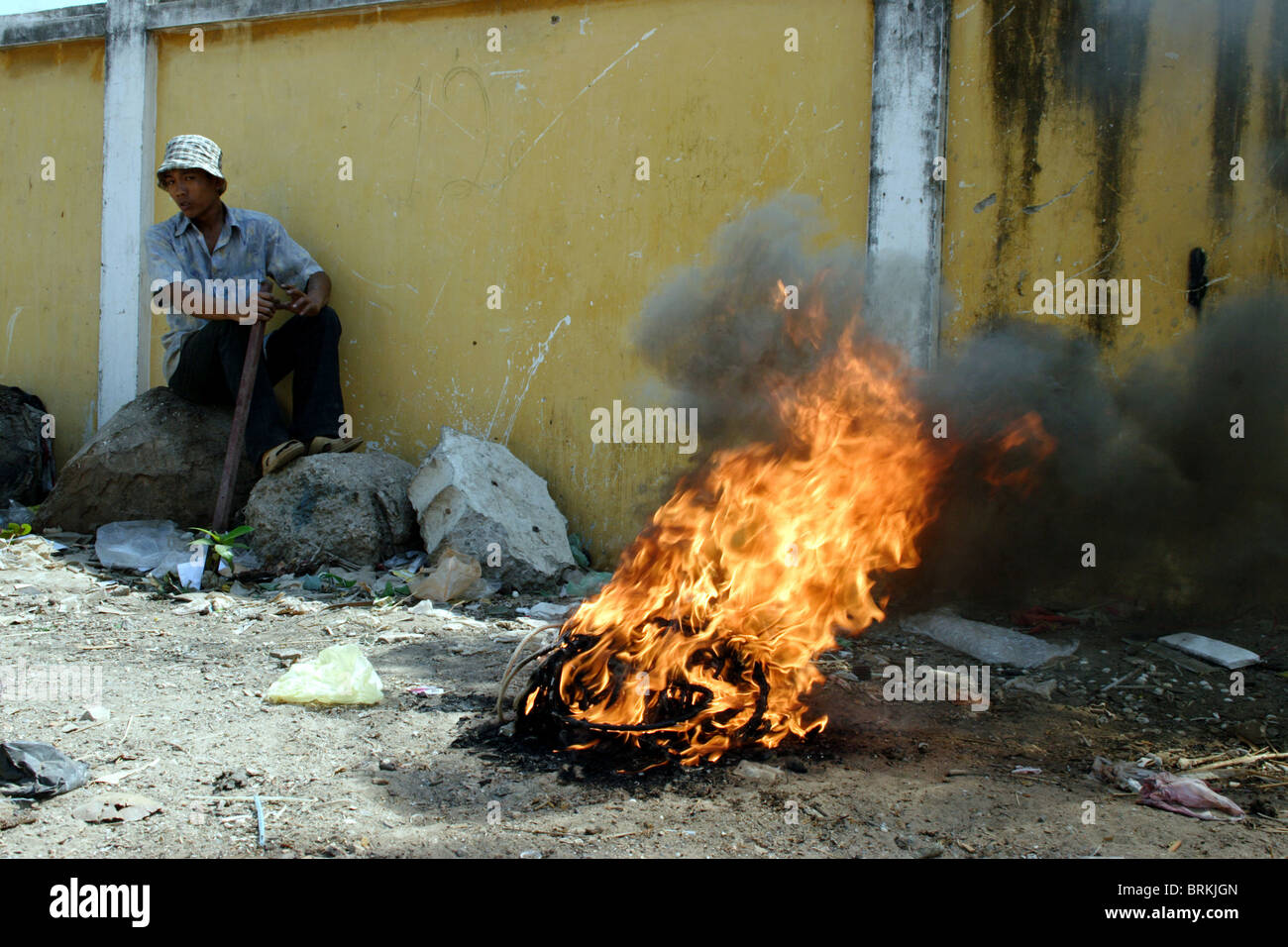 A burning rubber tire spews toxic smoke into the air as a man relaxes