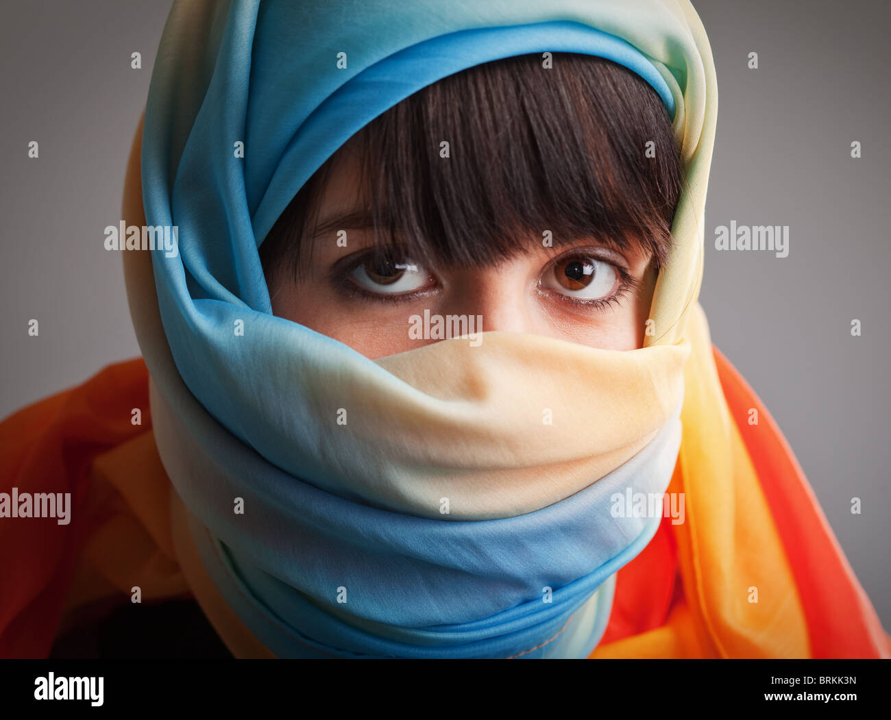Brunette girl in multicolored head scarf; photographed on gray background Stock Photo