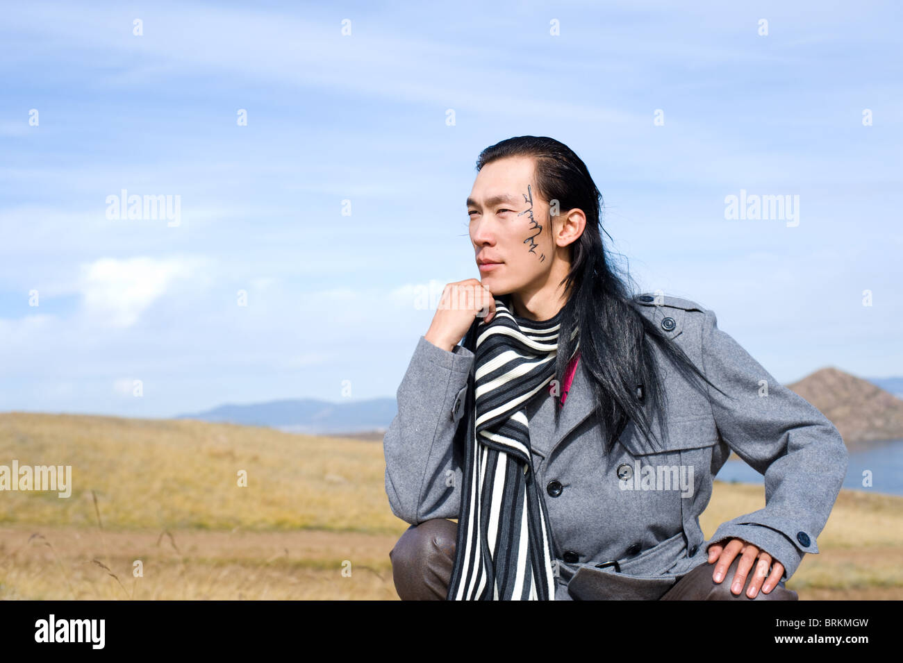 Young asian man in grey coat and striped black-and-white scarf. The tracery on his cheek is his name Chinghis in ancient Mongoli Stock Photo