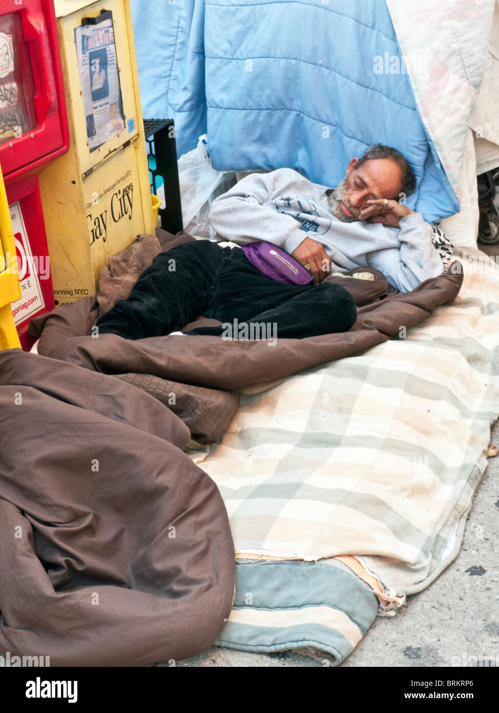 homeless Hispanic man with emaciated face wearing clean clothes lies peacefully asleep on clean bedding on New York sidewalk Stock Photo