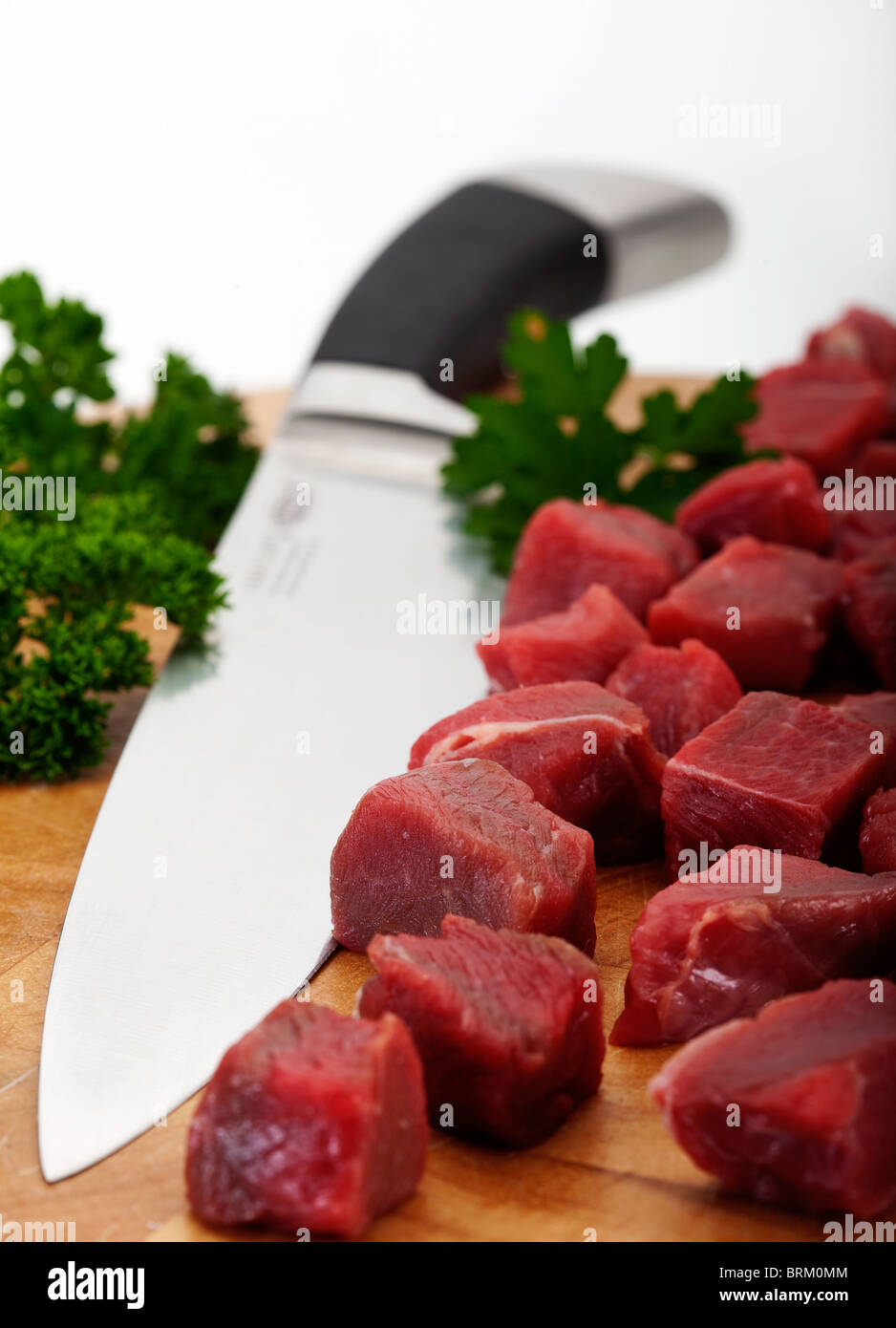Chopped braising steak on a chopping board with carving knife. Out of focus background Stock Photo