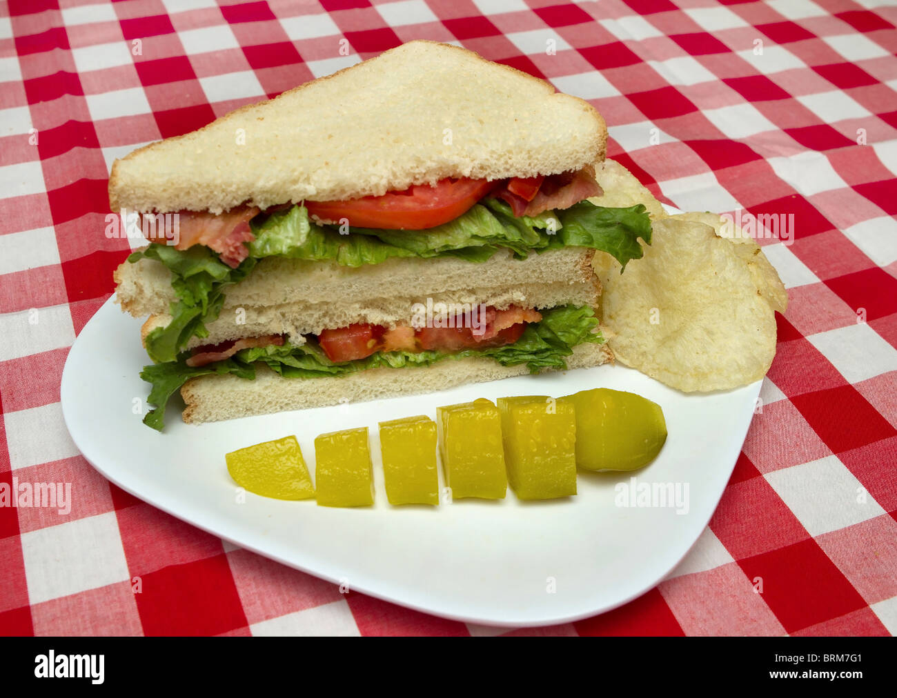 sliced BLT sandwich stacked on a white plate with pickle and chips Stock Photo