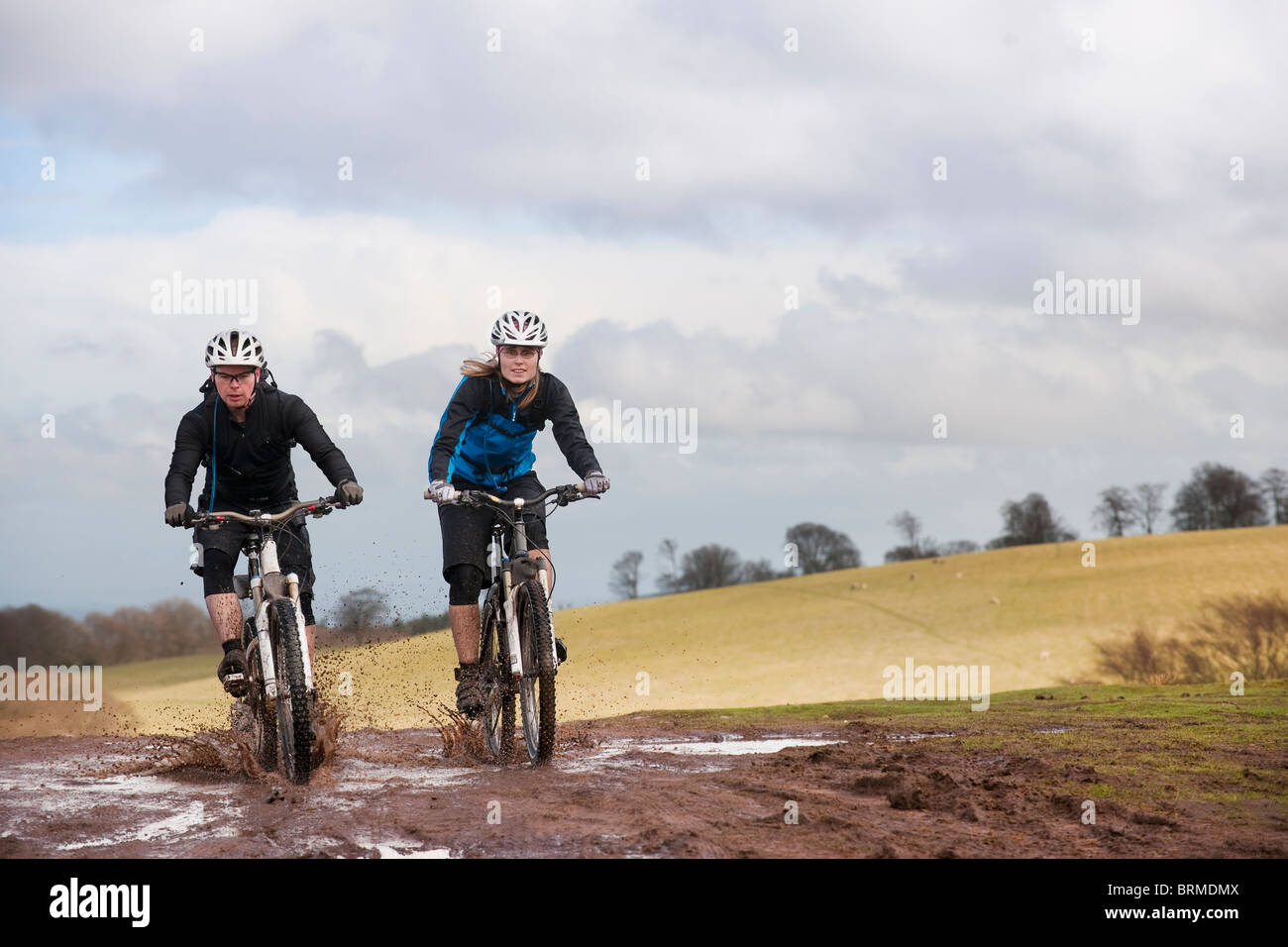Couple riding bike through muddy puddles Stock Photo