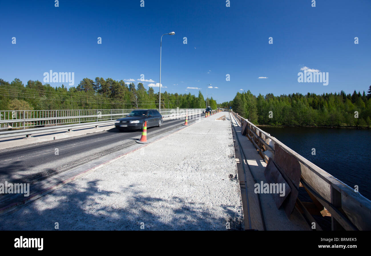 A car crossing a road bridge under repair . Half of the concrete deck is stripped open and waits recast and tarmac surface , Finland Stock Photo