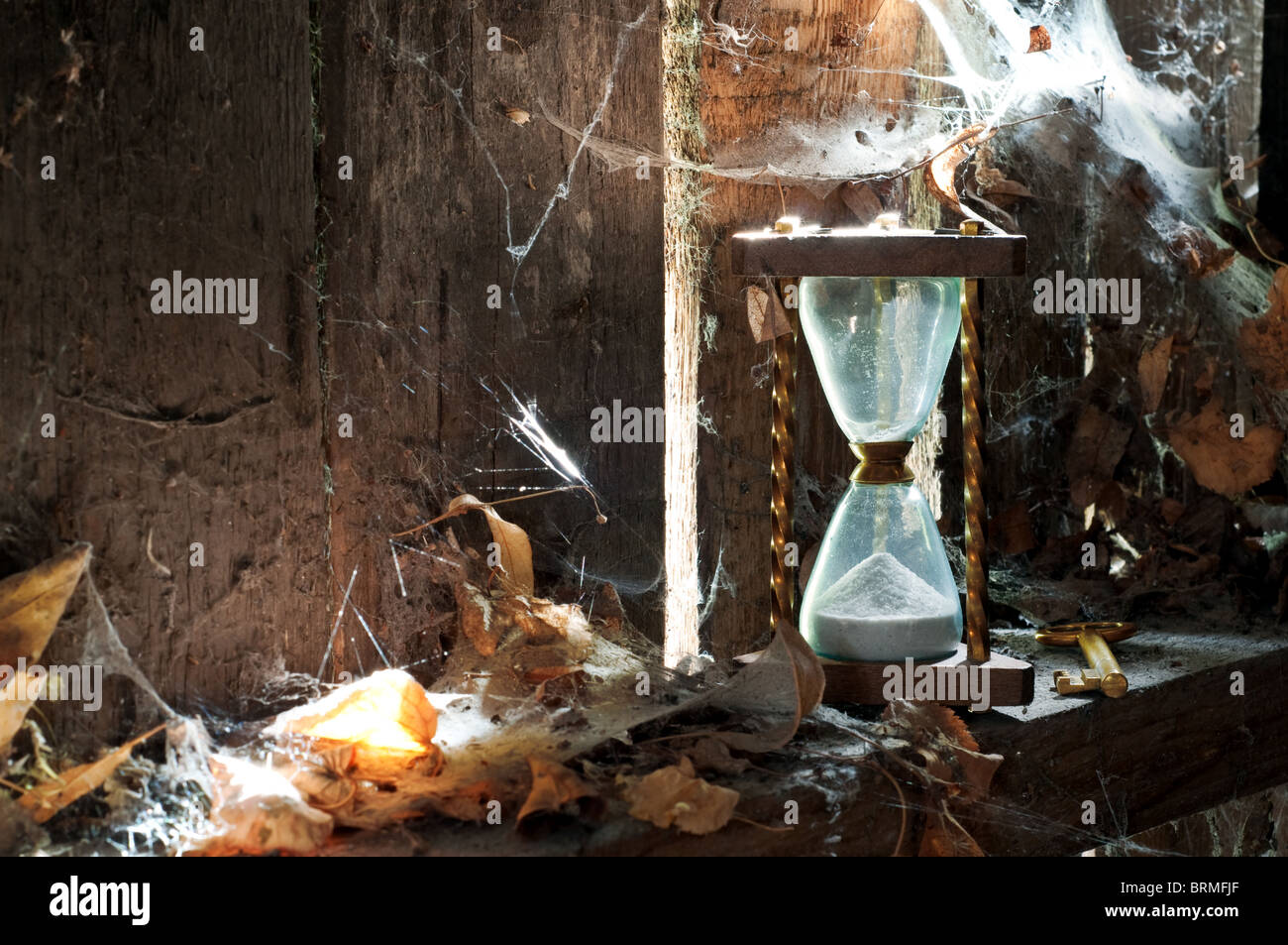 Past time concept - sandclock and a key forgotten in a dirty corner with leaves and cobwebs. Stock Photo