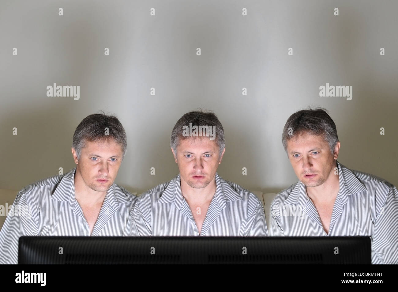 Three identical clones or triplets watching television or a computer screen together Stock Photo