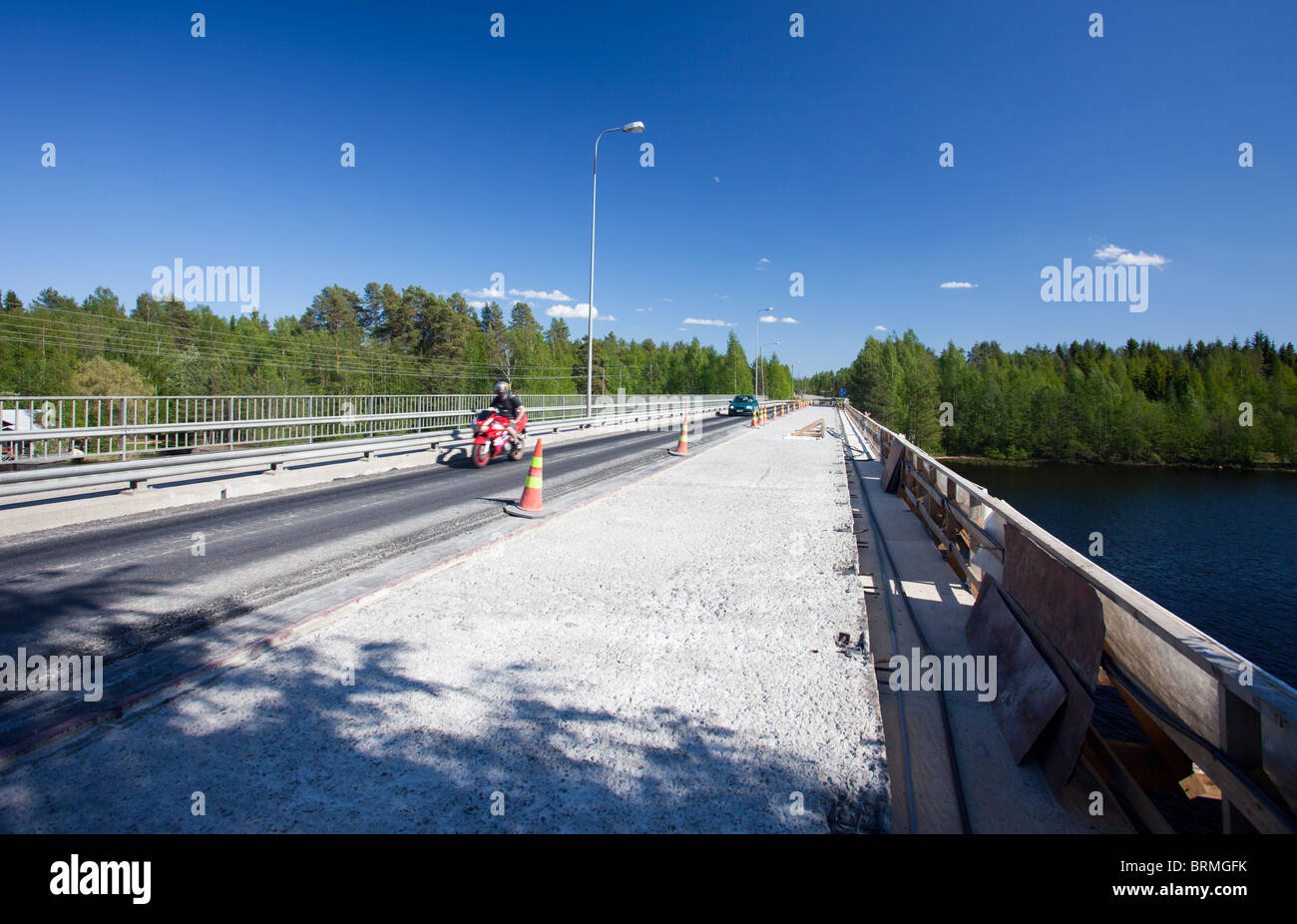 Biker crossing a road bridge where half of the deck is under repairs and asphalt has been stripped away , Finland Stock Photo