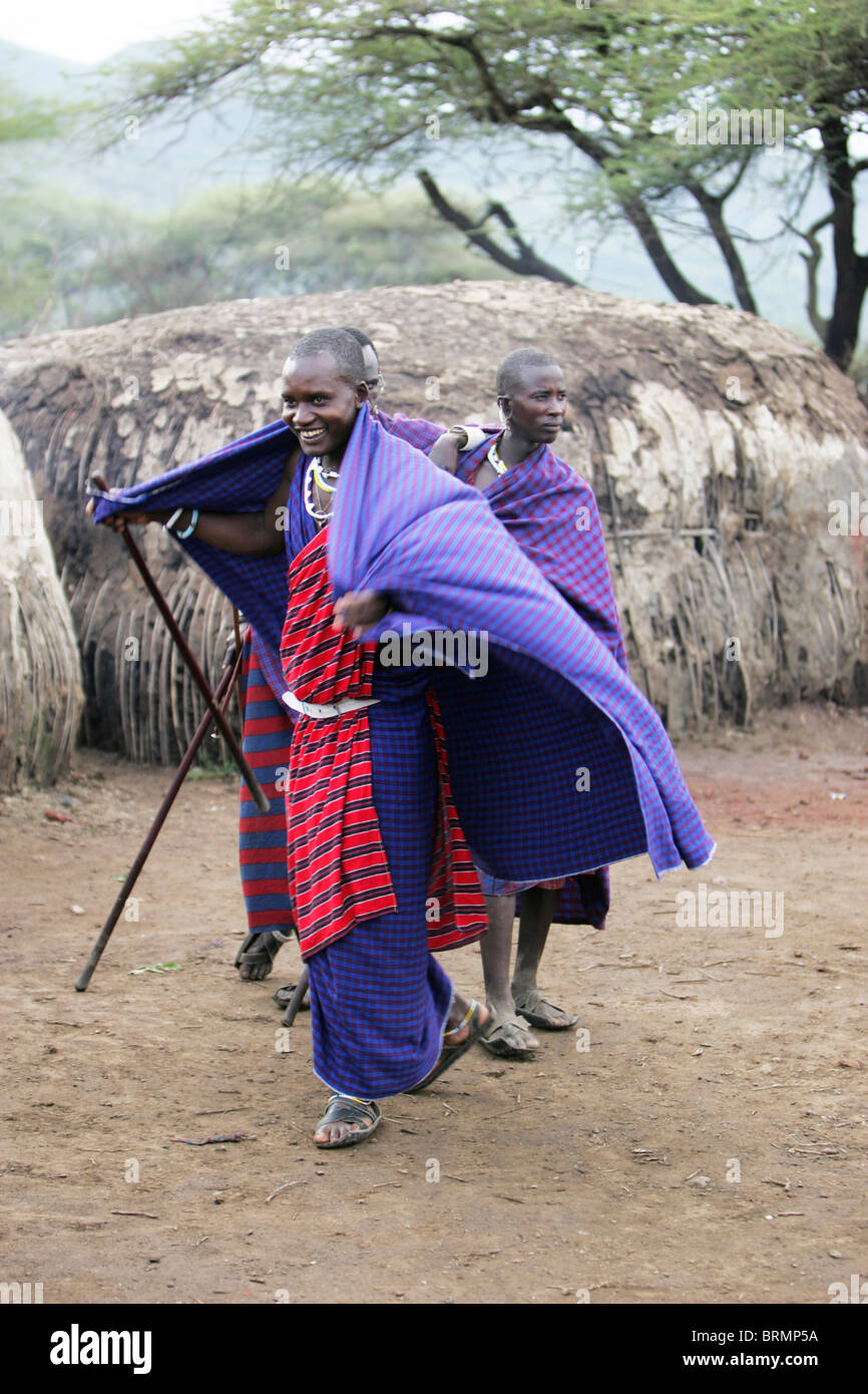 Maasai men standing amongst their mud huts wearing their shukas Stock Photo
