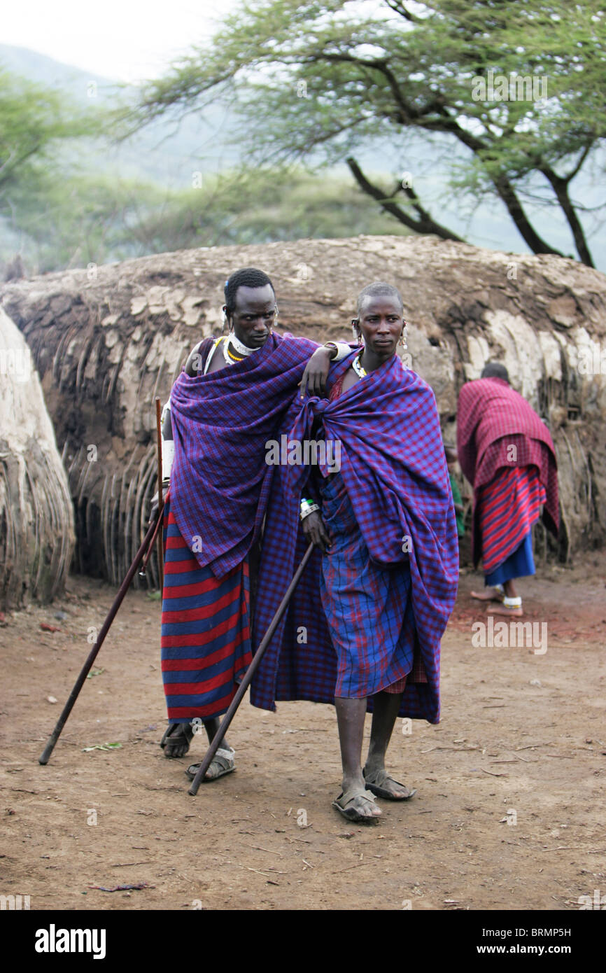 Maasai men standing amongst their mud huts wearing their shukas Stock Photo