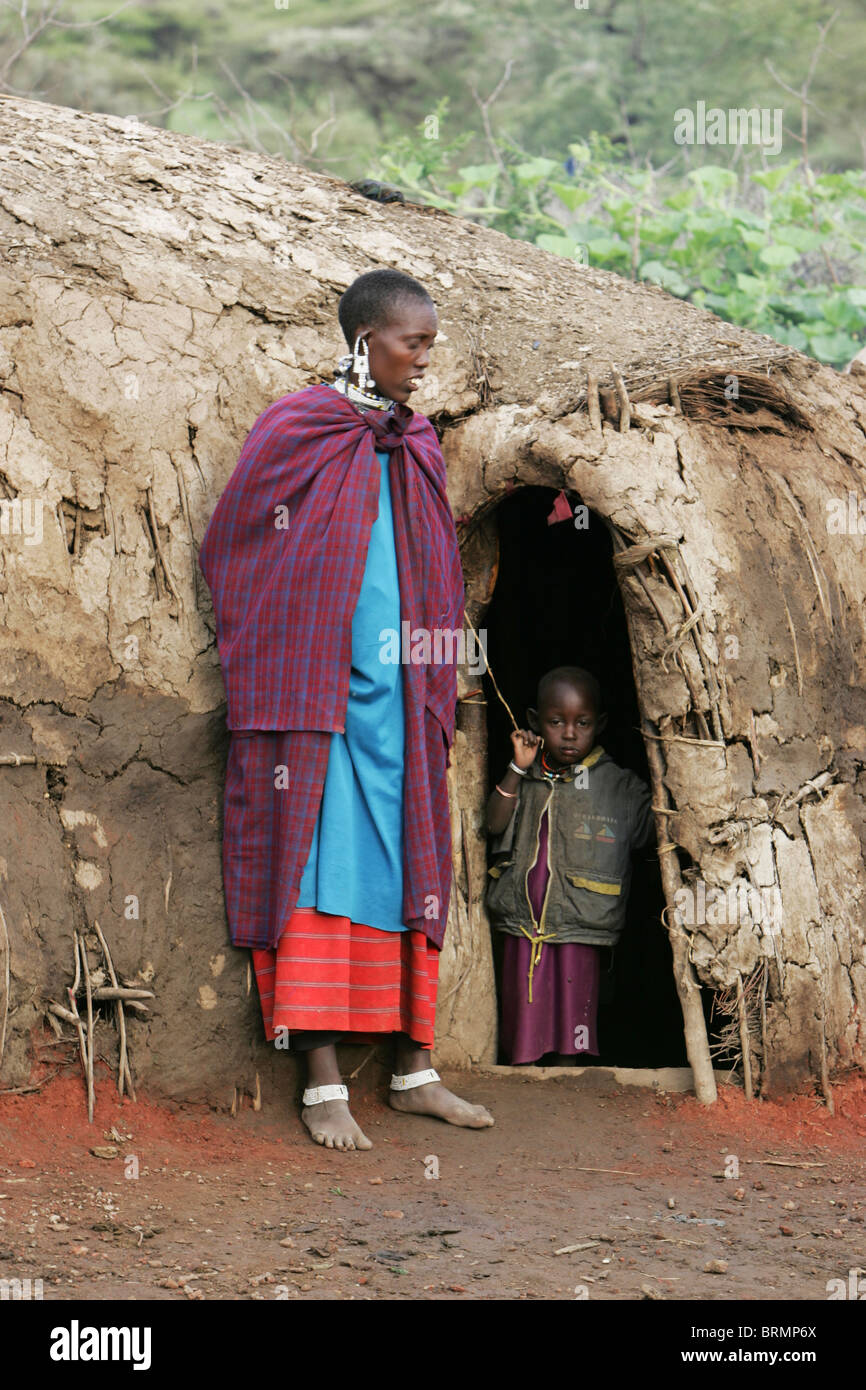 Maasai mother leaning against the wall of her hut and a toddler aged about 2 year old standing in the entrance of the home Stock Photo
