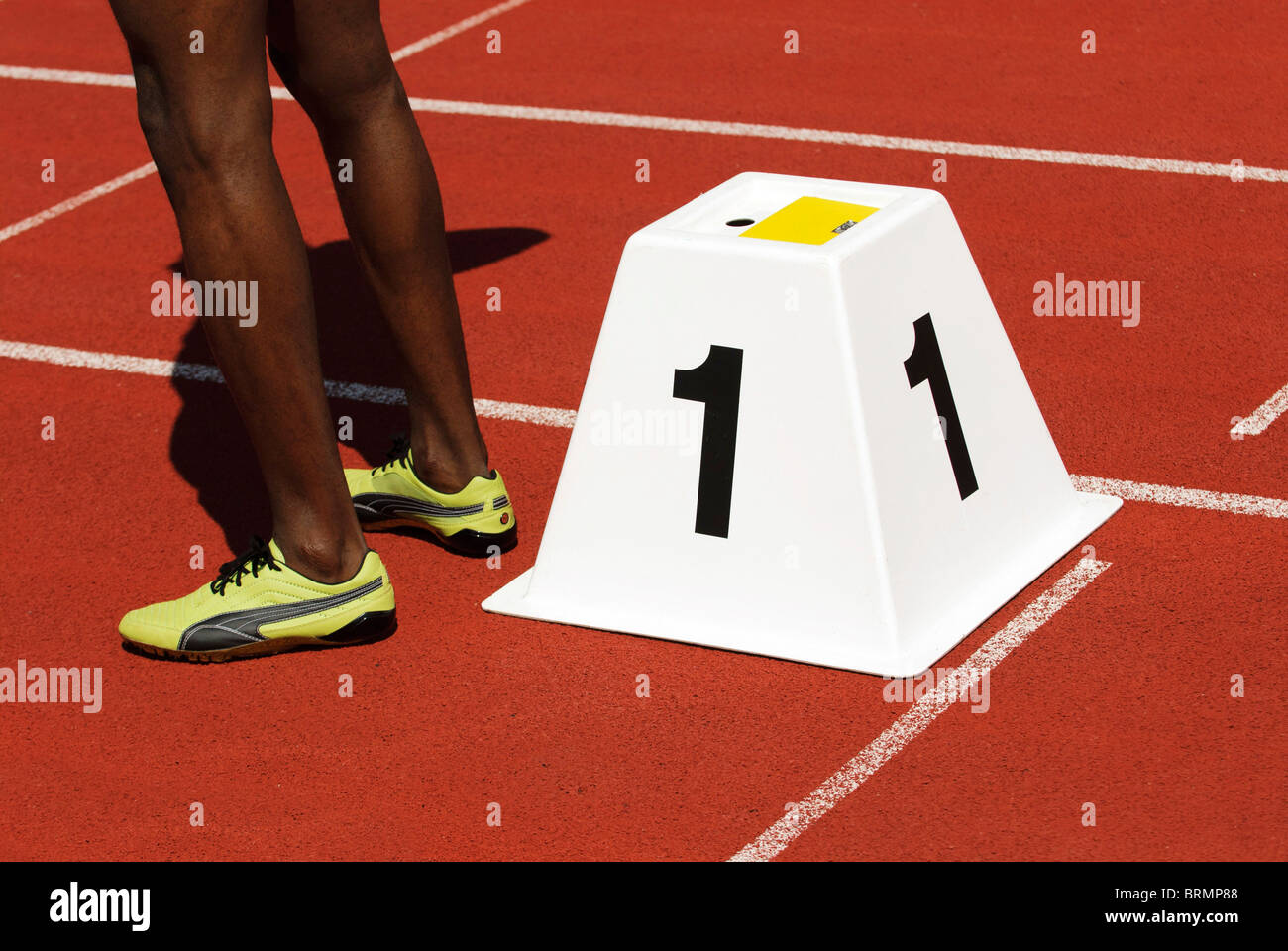legs of a male sprinter next to starting block number one on athletic track outside Stock Photo