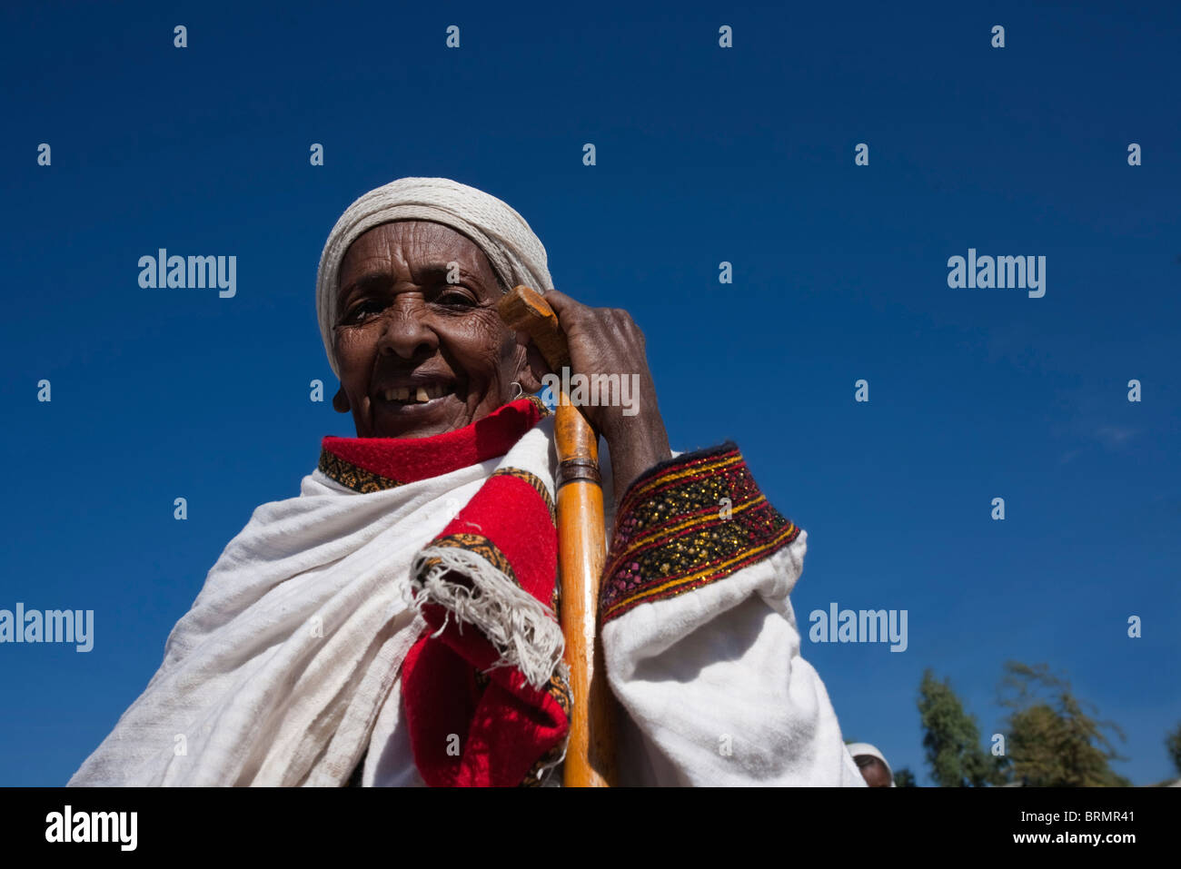 Portrait of a smiling elderly woman in a colourful, traditional gown resting her hand on a walking stick in Lalibela Stock Photo