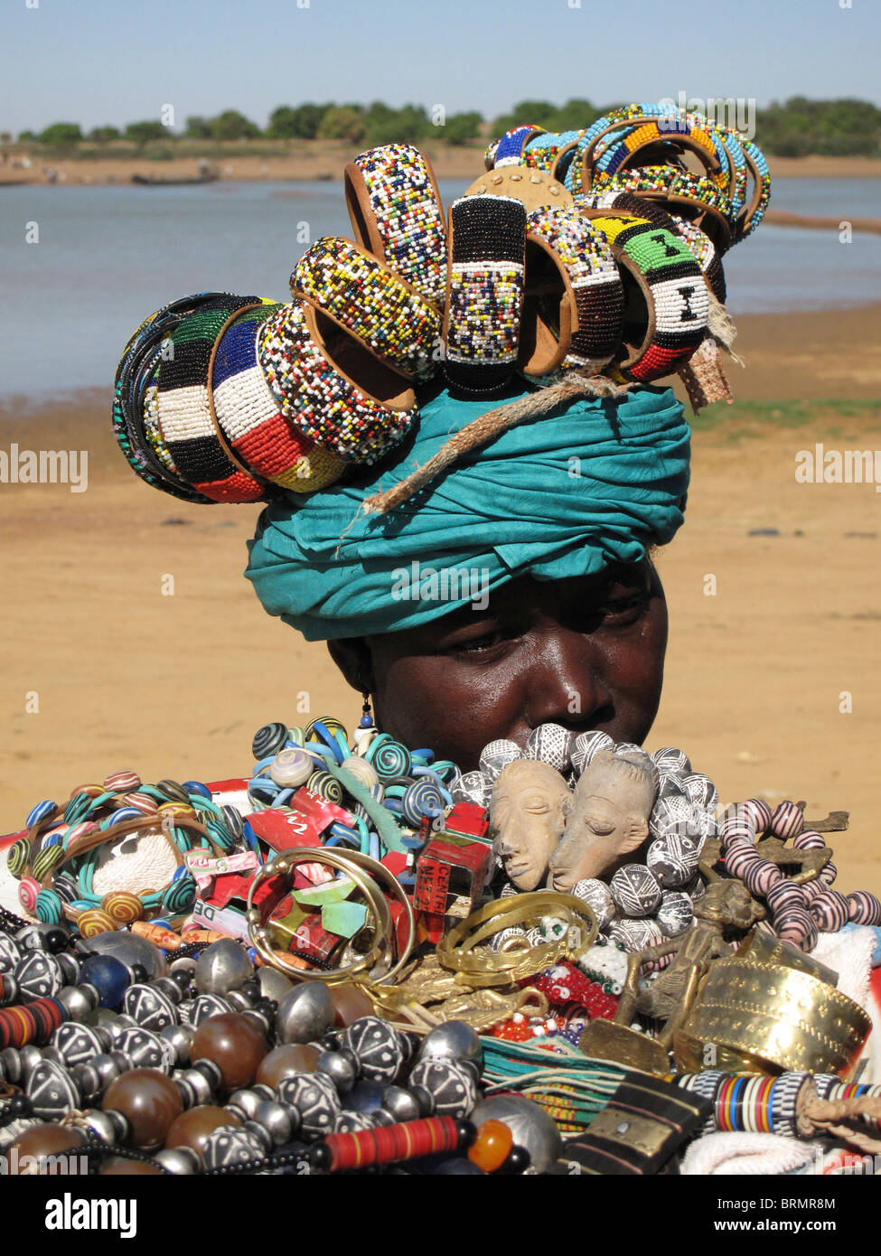 An African woman selling beaded necklaces and bracelets that she is balancing on her head Stock Photo
