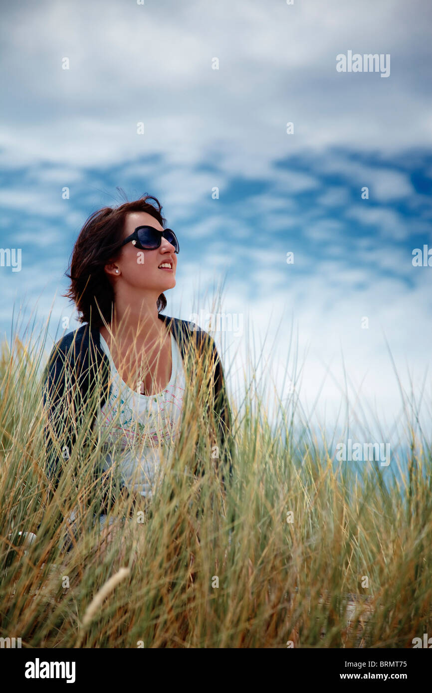 Woman wearing sunglasses sitting in long grass looking up at the sky Stock Photo