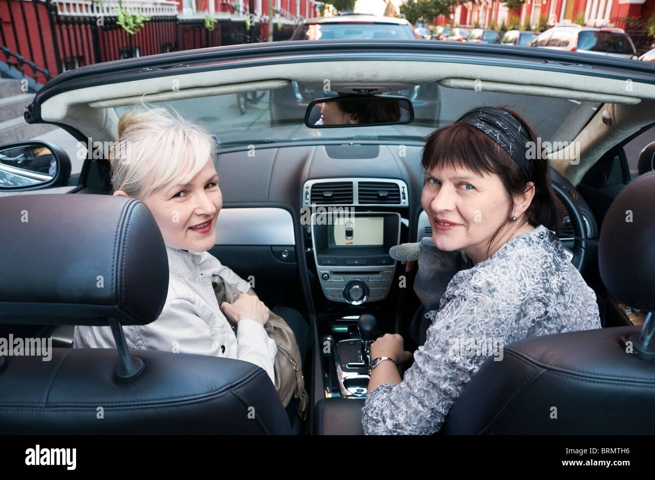 Portrait, front of two mature, one dark and blond hair women friends sitting in open top convertible car in London, England, UK Stock Photo