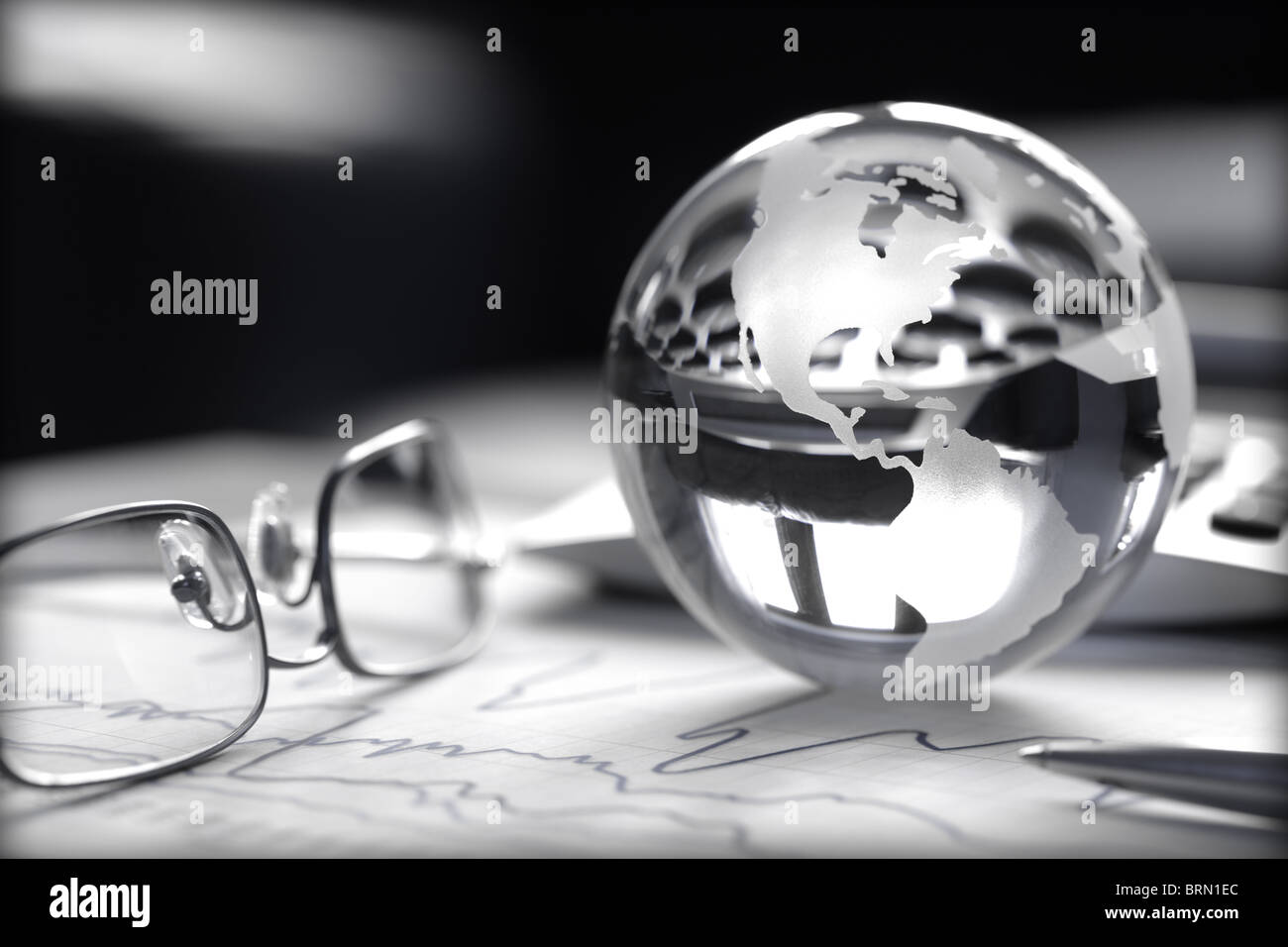 Toned image of glass globe with stock charts, calculator and spectacles Stock Photo