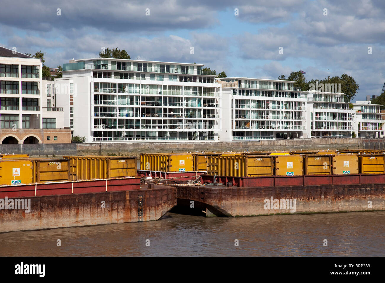 Waste barges on the river Thames opposite new apartment buildings Stock