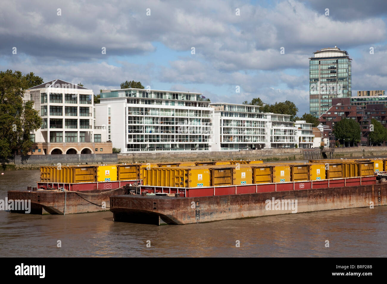 Waste barges on the river Thames opposite new apartment buildings Stock