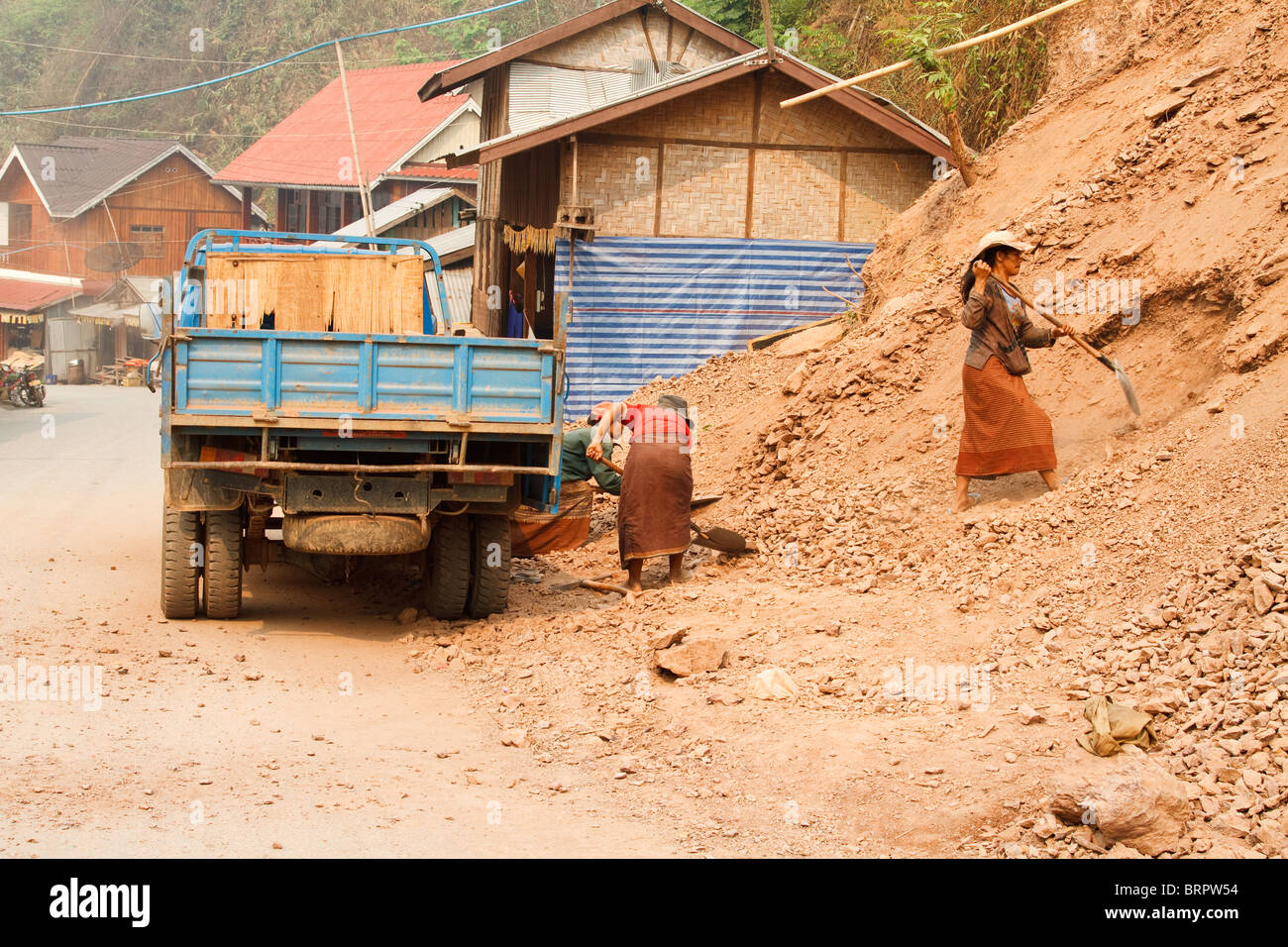 Two minority women shovel dirt into a truck at a construction site in Pak Beng, Laos Stock Photo