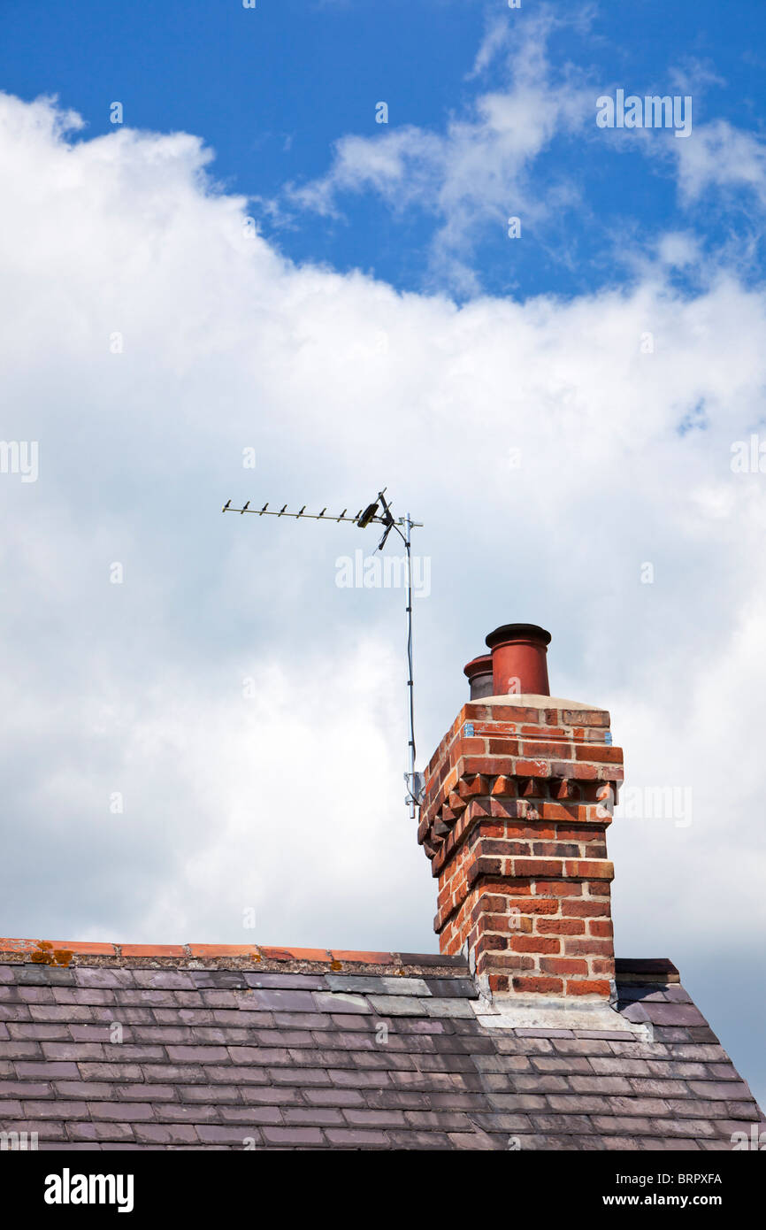 TV aerial on house slate roof with a red brick chimney stack Stock Photo