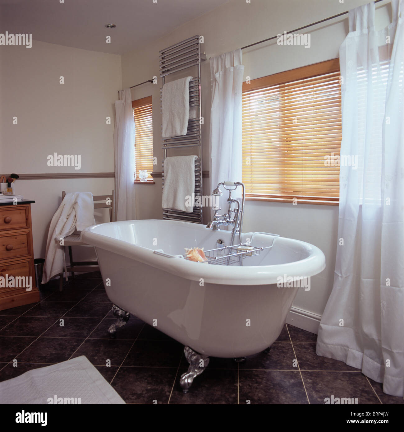 Roll-top bath in front of window with slatted wooden blind and white  curtains in country bathroom Stock Photo - Alamy