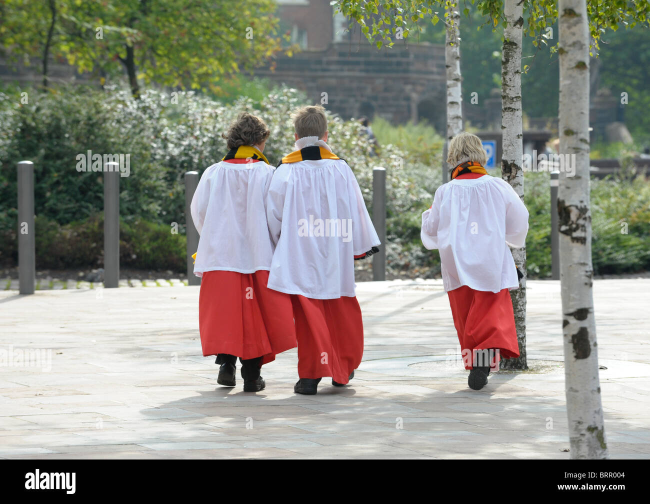 Three choir boys in robes coming back from a Wolves match wearing scarves  walking across a sunlit pavement by St Peter's Stock Photo - Alamy