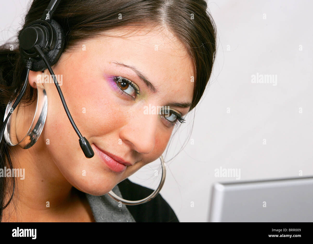 a smiling, young, beautiful female CSR representative using a telephone ...