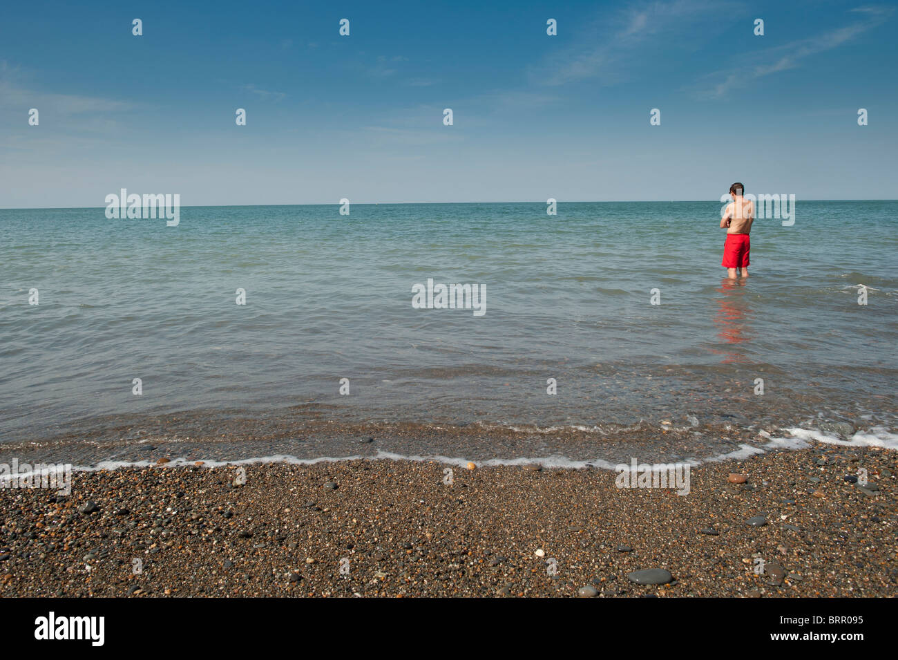 A man on holiday standing alone in the sea wearing red shorts, Aberystwyth wales UK Stock Photo
