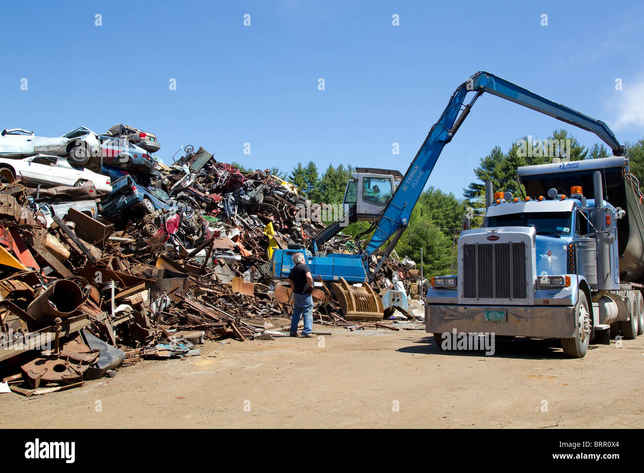 Crane loading semi truck with crushed cars, scrap metal automobiles, at