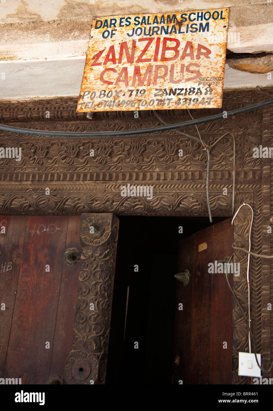 Close-up of wooden door with a rusted signboard advertising the Dar Es Salaam School of Journalism, Zanzibar campus Stock Photo