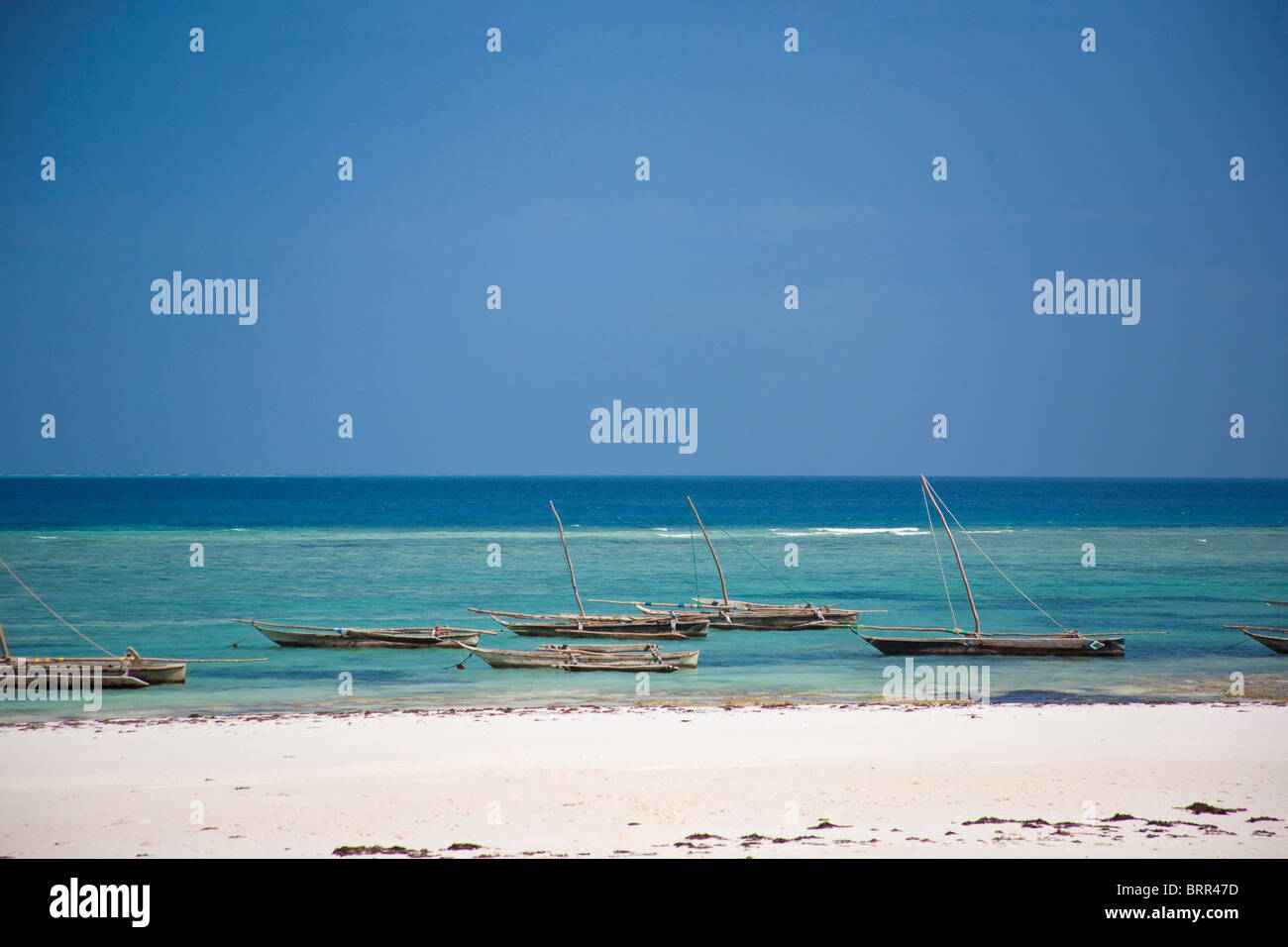Beach scene with outrigger fishing boats moored in shallow water off Mnemba Island Stock Photo
