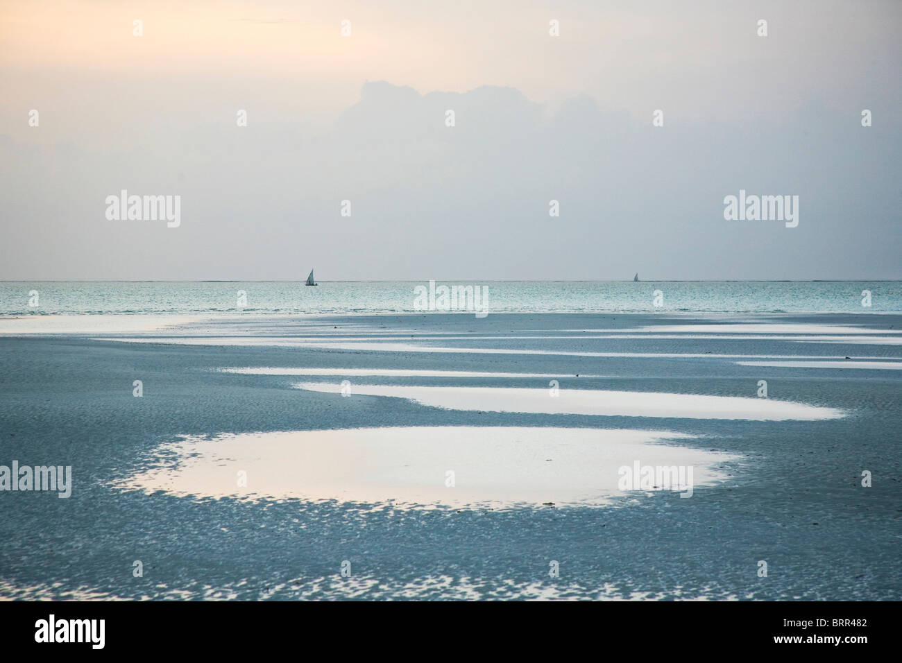 Deserted island beach at dawn with distant dhows on the sea Stock Photo