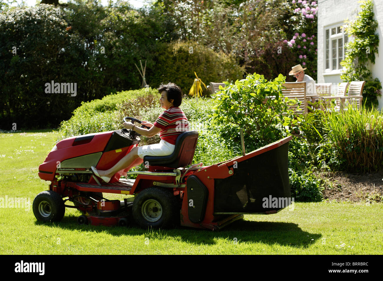 retired older woman using a ride on lawnmower Stock Photo
