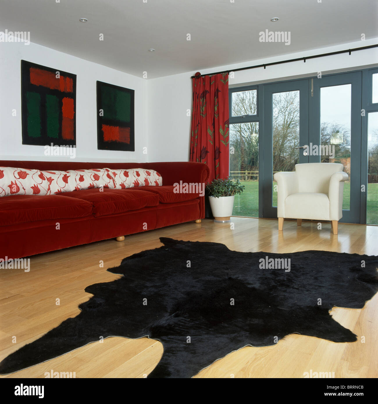 Black faux-animal-skin rug on wooden floor in modern living room with long  red sofa and French windows Stock Photo - Alamy