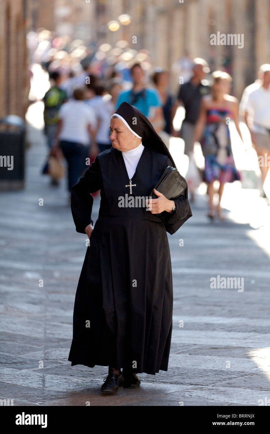 A Roman Catholic nun walking along a busy street amongst other people busy shopping at San Gimignano, Tuscany Italy Stock Photo