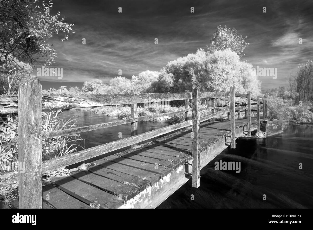 Infra Red wooden bridge over River Test dark sky white leaves black and white Stock Photo