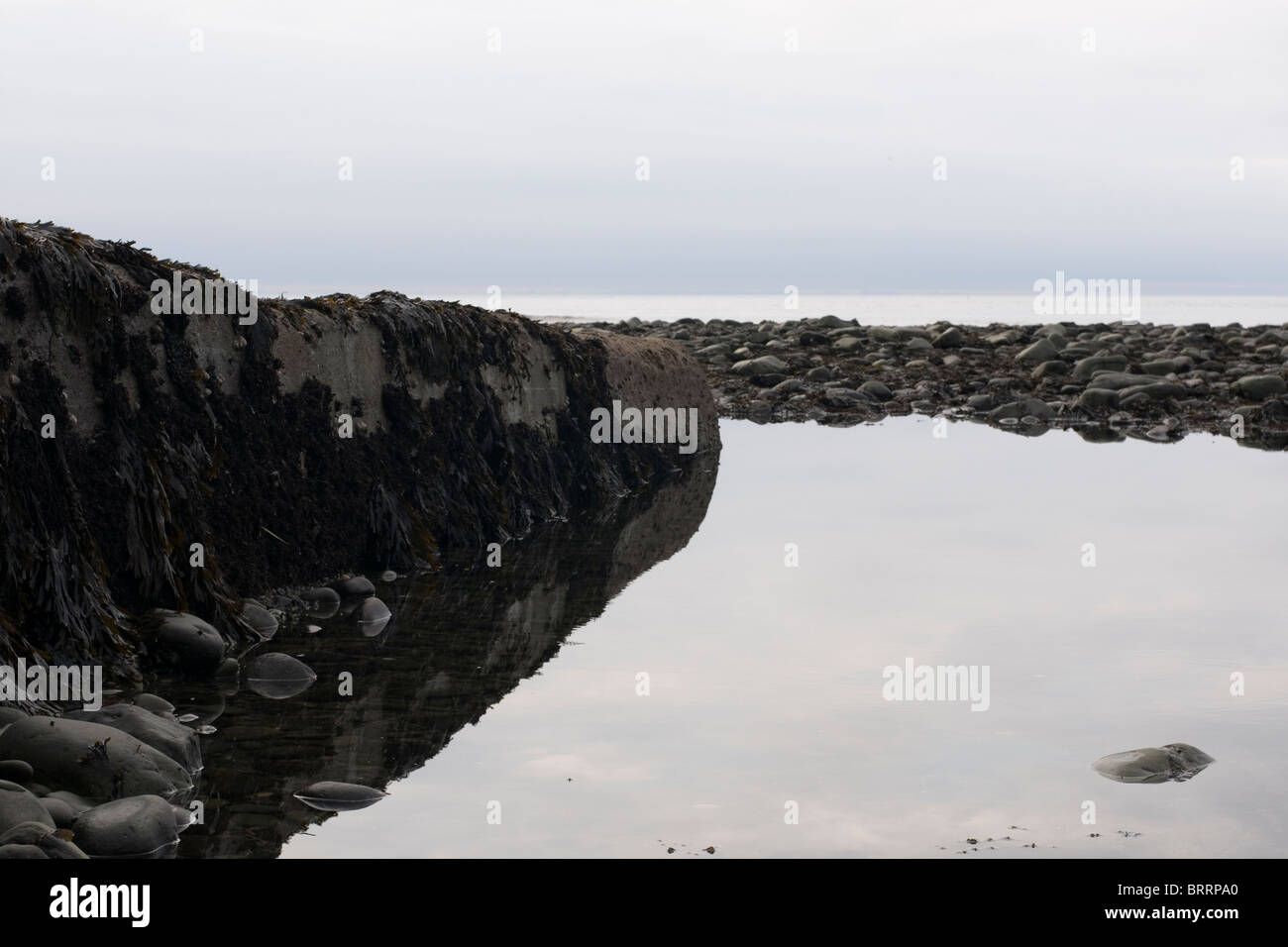 A scenic image of south beach in Aberystwyth with the sky and clouds reflecting in the water in the rock pools. Stock Photo
