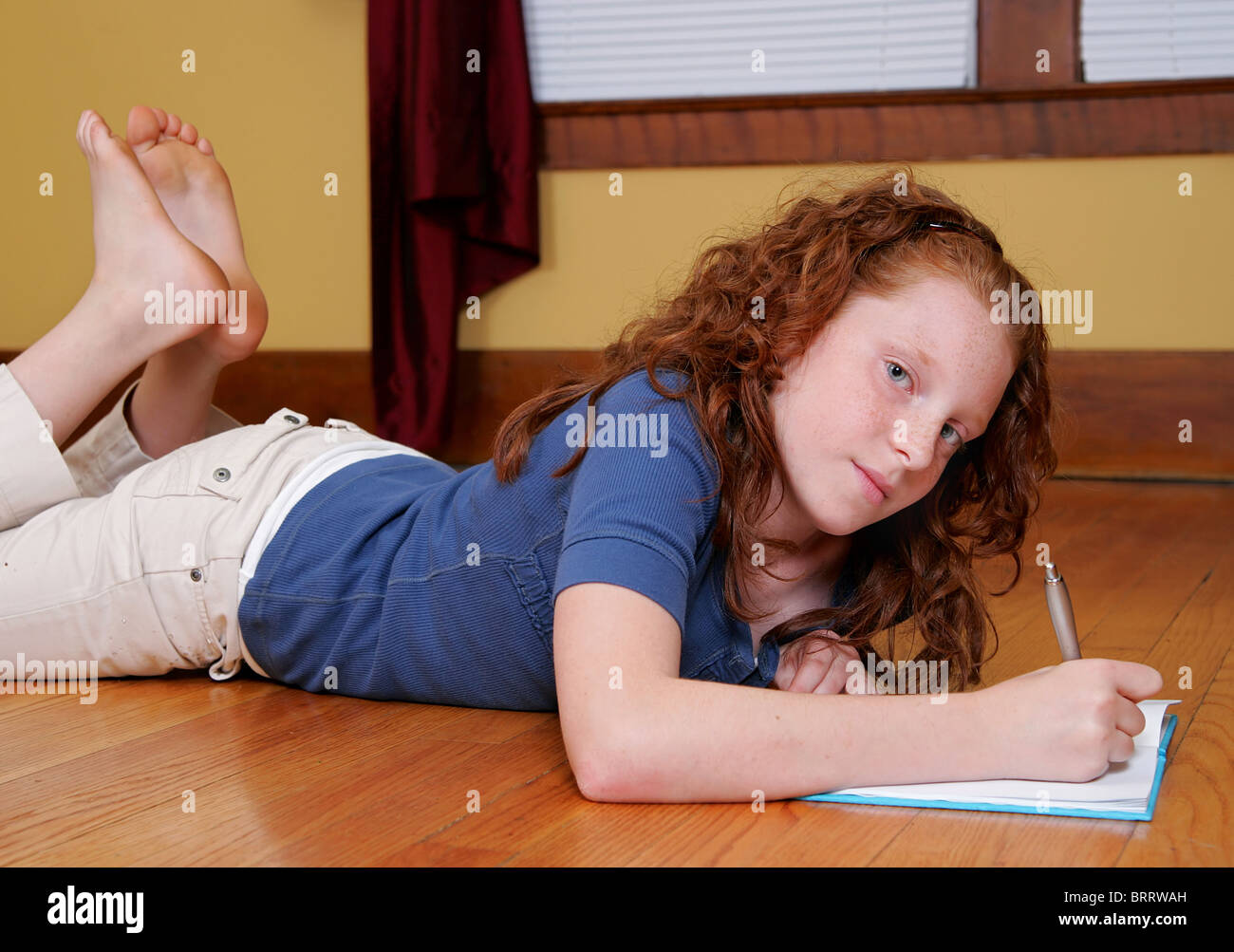 a young female child laying on the hardwood floor and writing in a