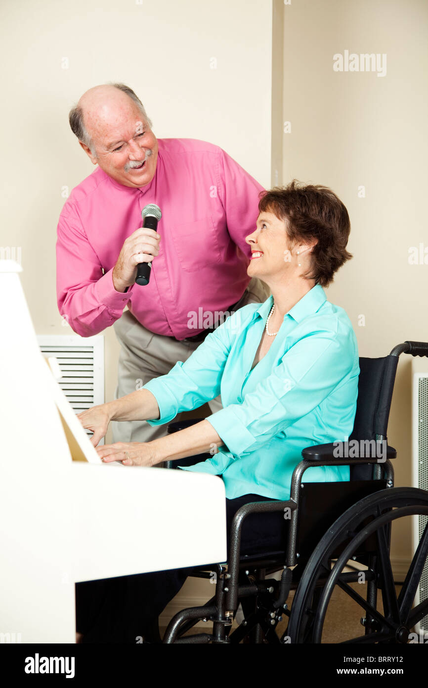 Musician in wheelchair playing the piano while her husband sings Stock