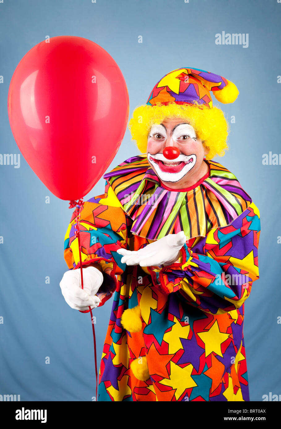 Happy birthday clown holding out a red balloon for you Stock Photo - Alamy
