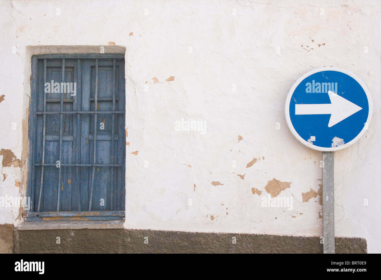 Blue keep right sign against peeling whitewashed wall and old blue window Stock Photo