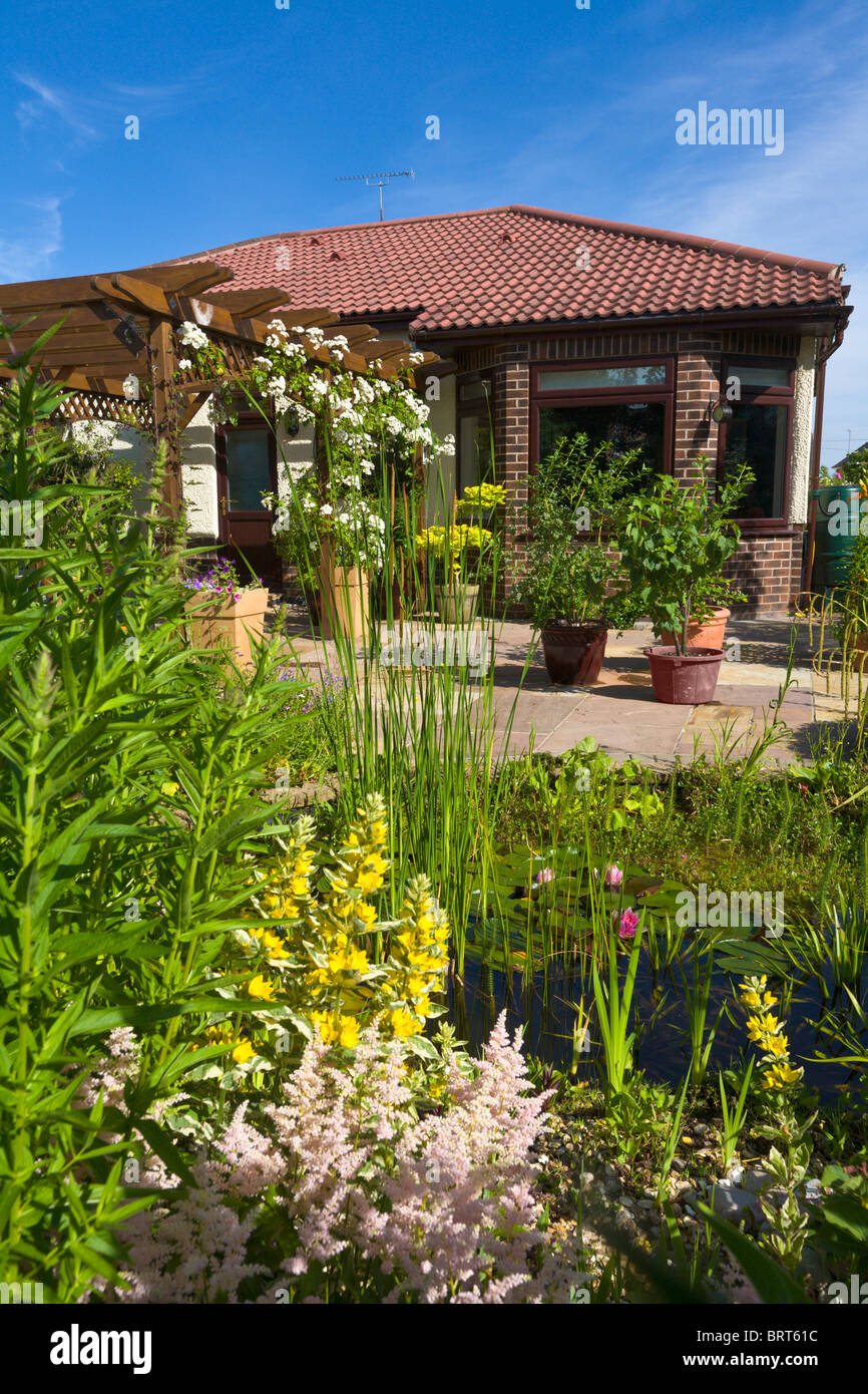 Back garden of bungalow overlooking pond with pergola and patio