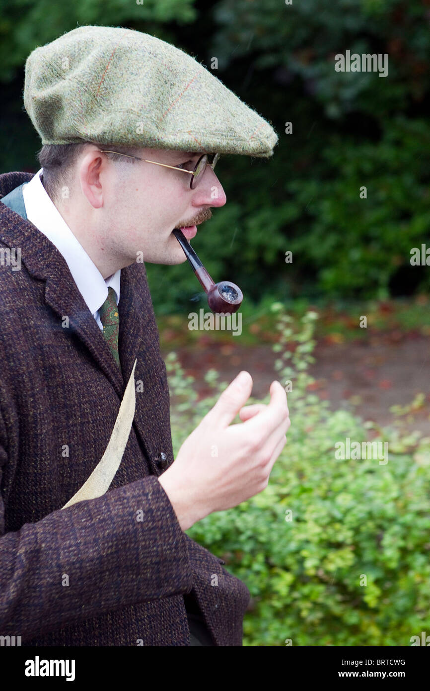 Mustached man in flat cap with spectacles smoking straight stem tobacco pipe 1940s attire Stock Photo