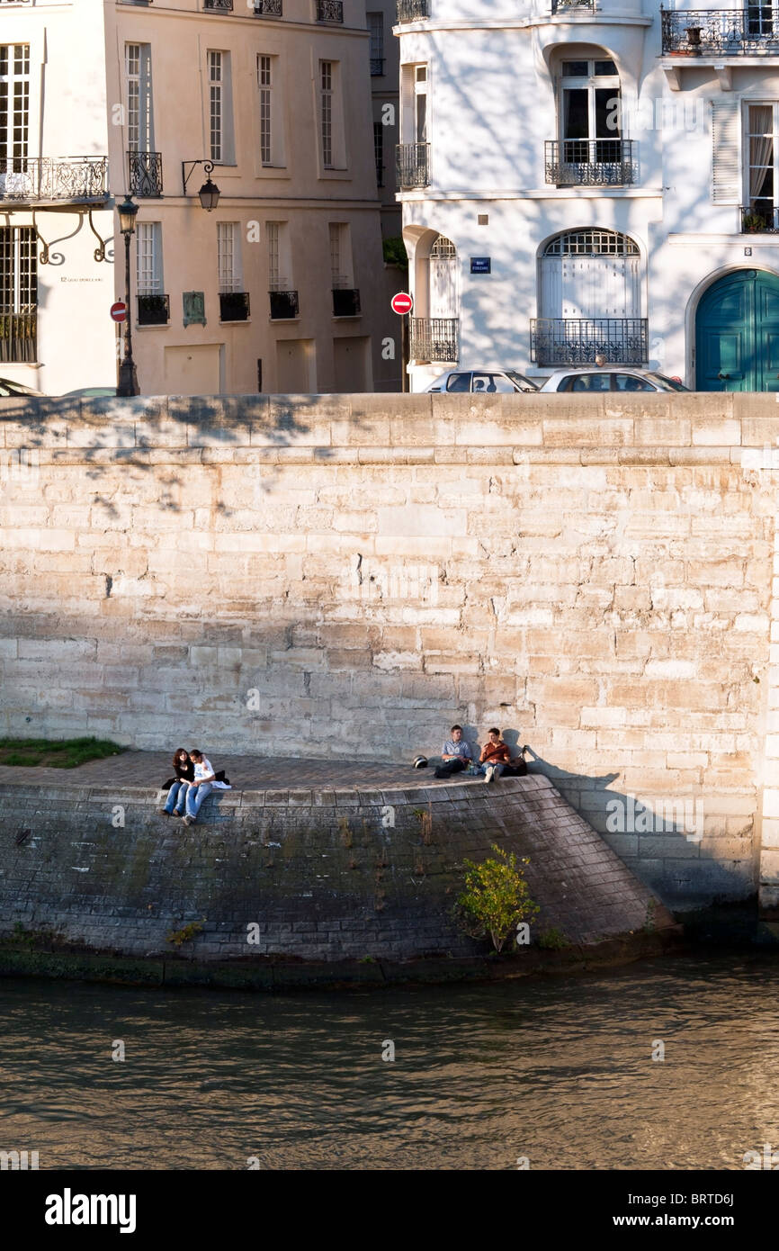 a courting couple & 2 young men sharing a sandwich enjoy late afternoon sun on Quai d'Orleans on warm autumn afternoon in Paris Stock Photo