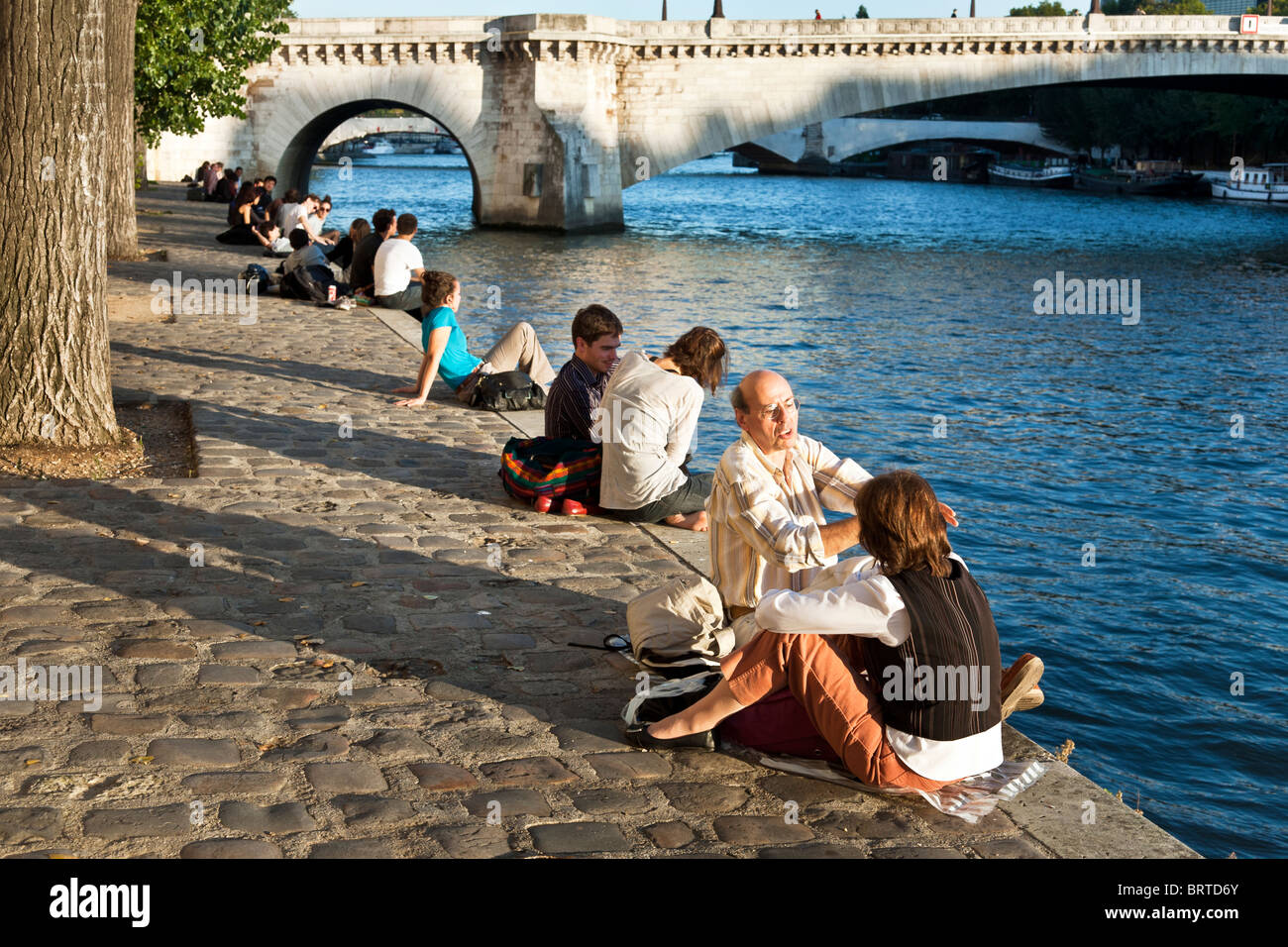 Parisian people cluster along the edge of Quai d'Orleans north of Pont de la Tournelle on a warm autumn afternoon in Paris Stock Photo