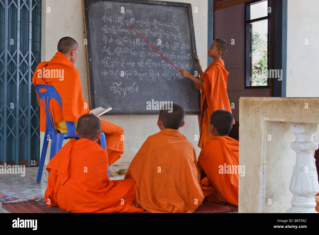 A Burmese novice monk  stands at a blackboard reviewing what his teacher has written Stock Photo