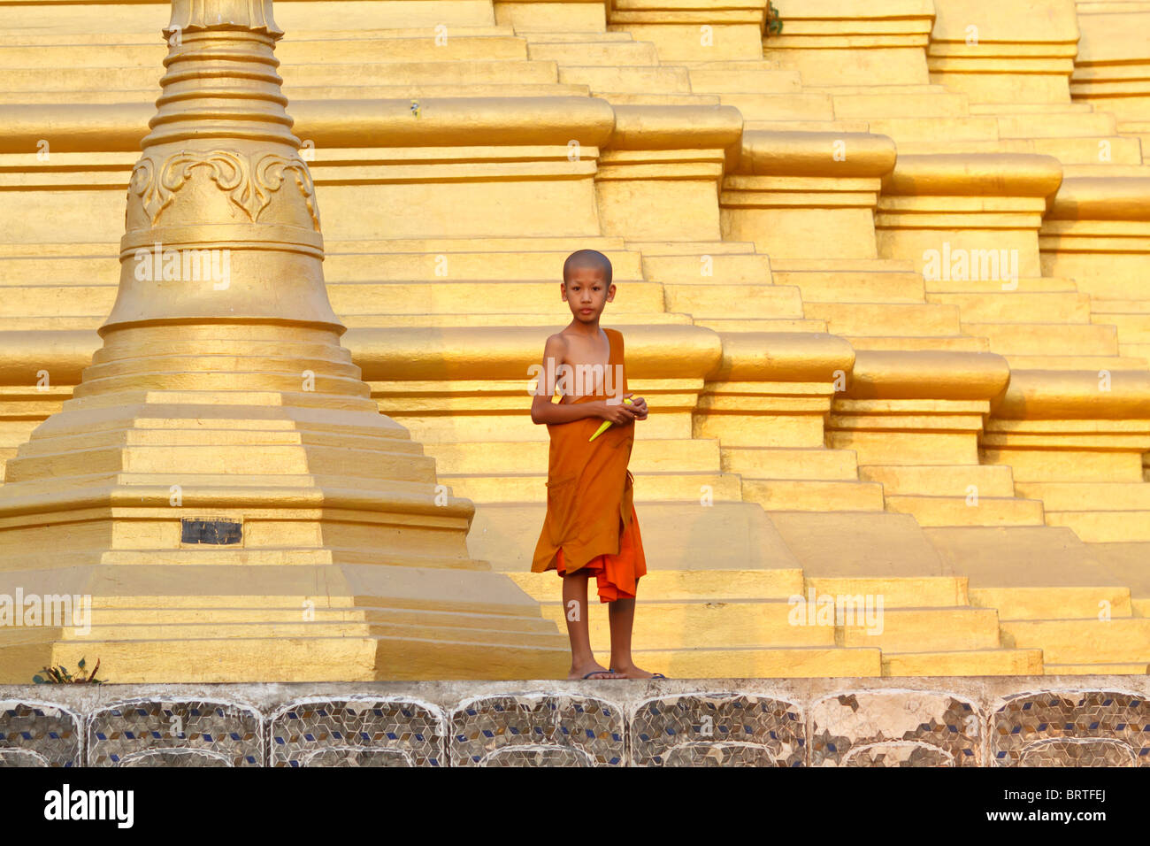 A young Thai monk stands on the base of a stupa Stock Photo