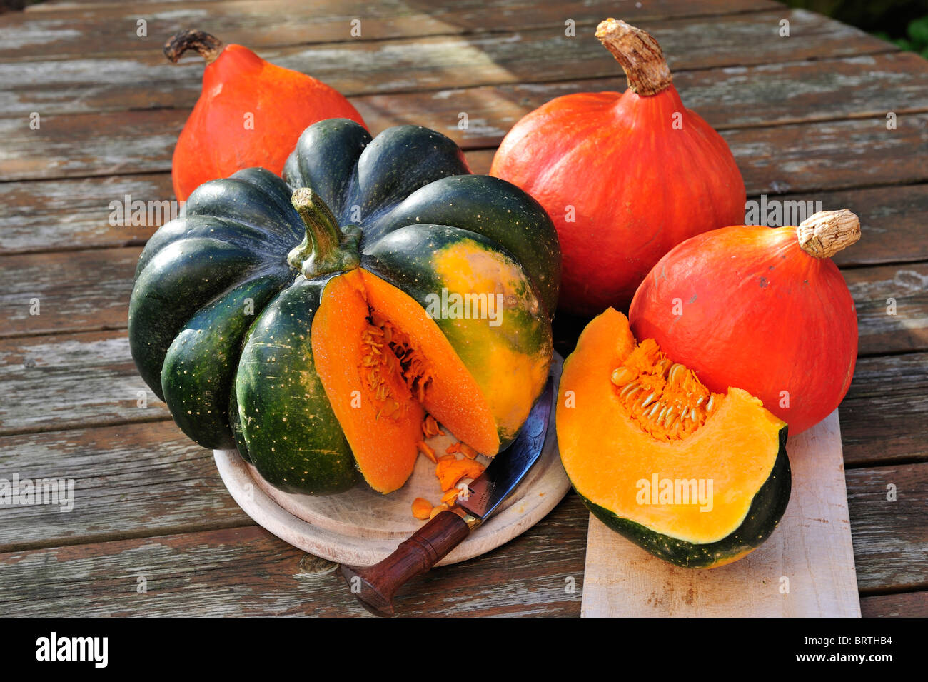 Cut of green Acorn squash and orange Hokkaido pumpkins on a wooden board. Stock Photo